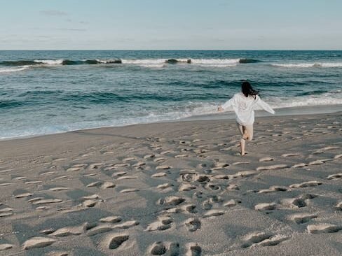 A woman runs joyfully on a beautiful sandy beach under a clear sky. Symbolizing natural healthy living.